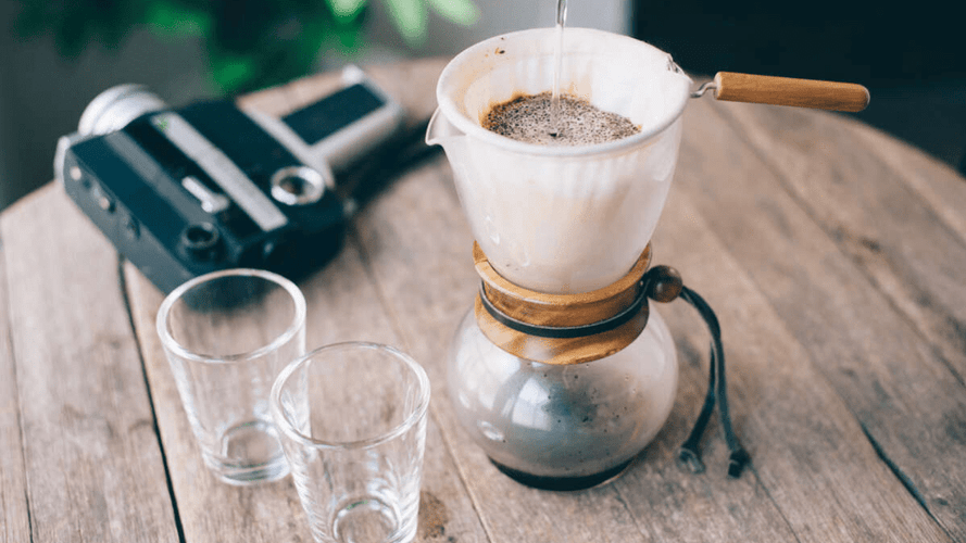 Ein Hario Drip Pot Woodneck steht auf einem Tisch und brüht gerade frischen Kaffee.