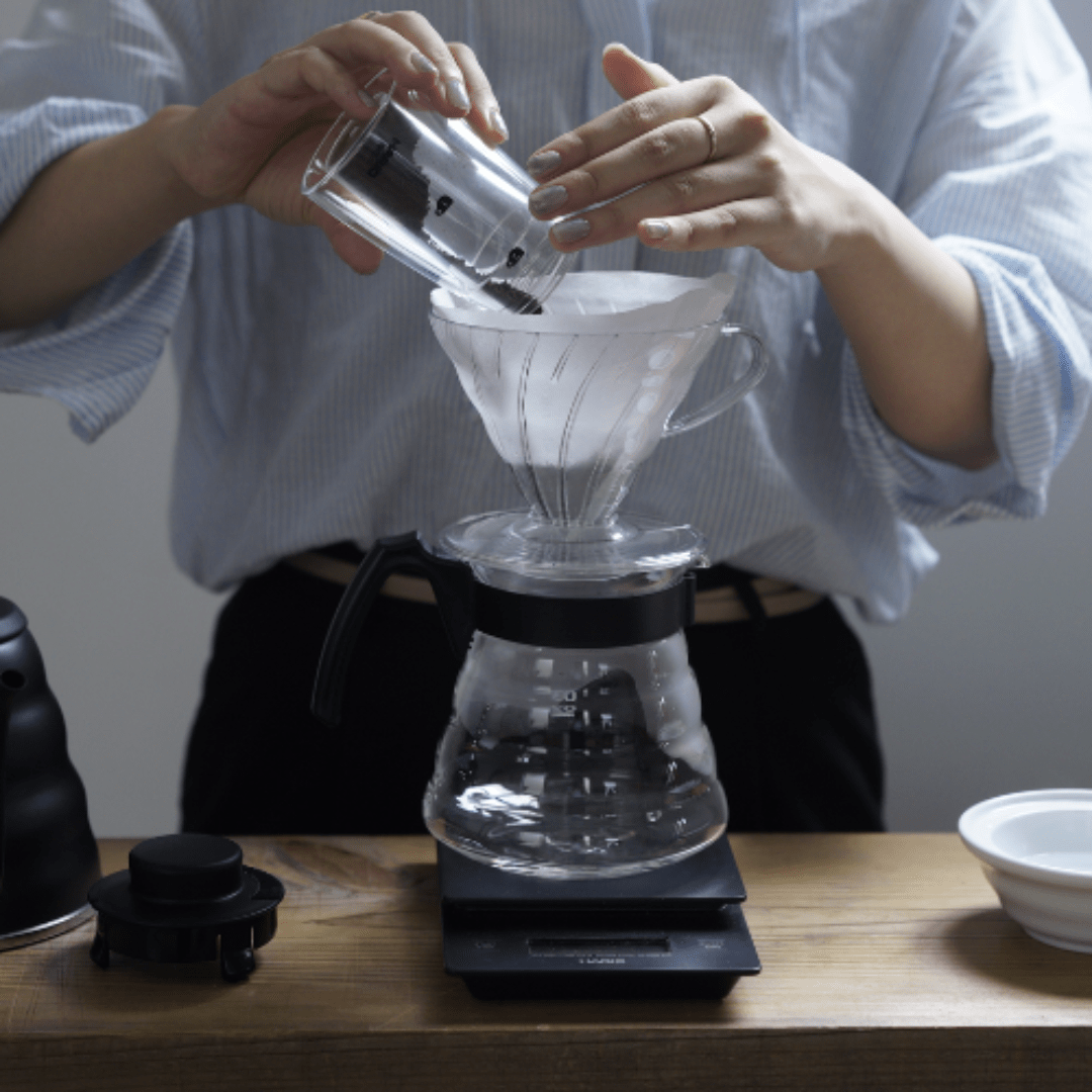 Ein Mann füllt frisches Kaffeepulver in den Filter des Hario V60 Craft Coffee Makers