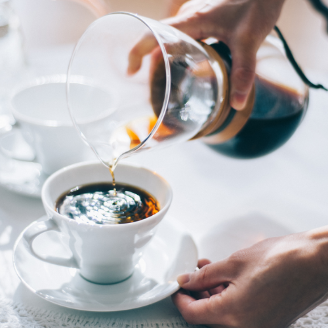 Eine Hand gießt frischen Kaffee von dem Hario Drip Pot "Woodneck" in eine Tasse