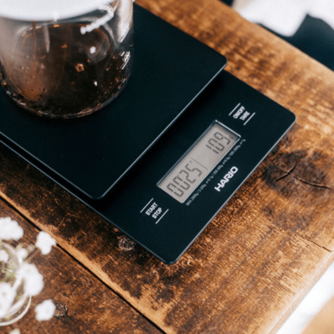 Ein Bild von der Kaffeewaage V60 Drip Scale von Hario, welche gerade Kaffee in einem Behälter wiegt