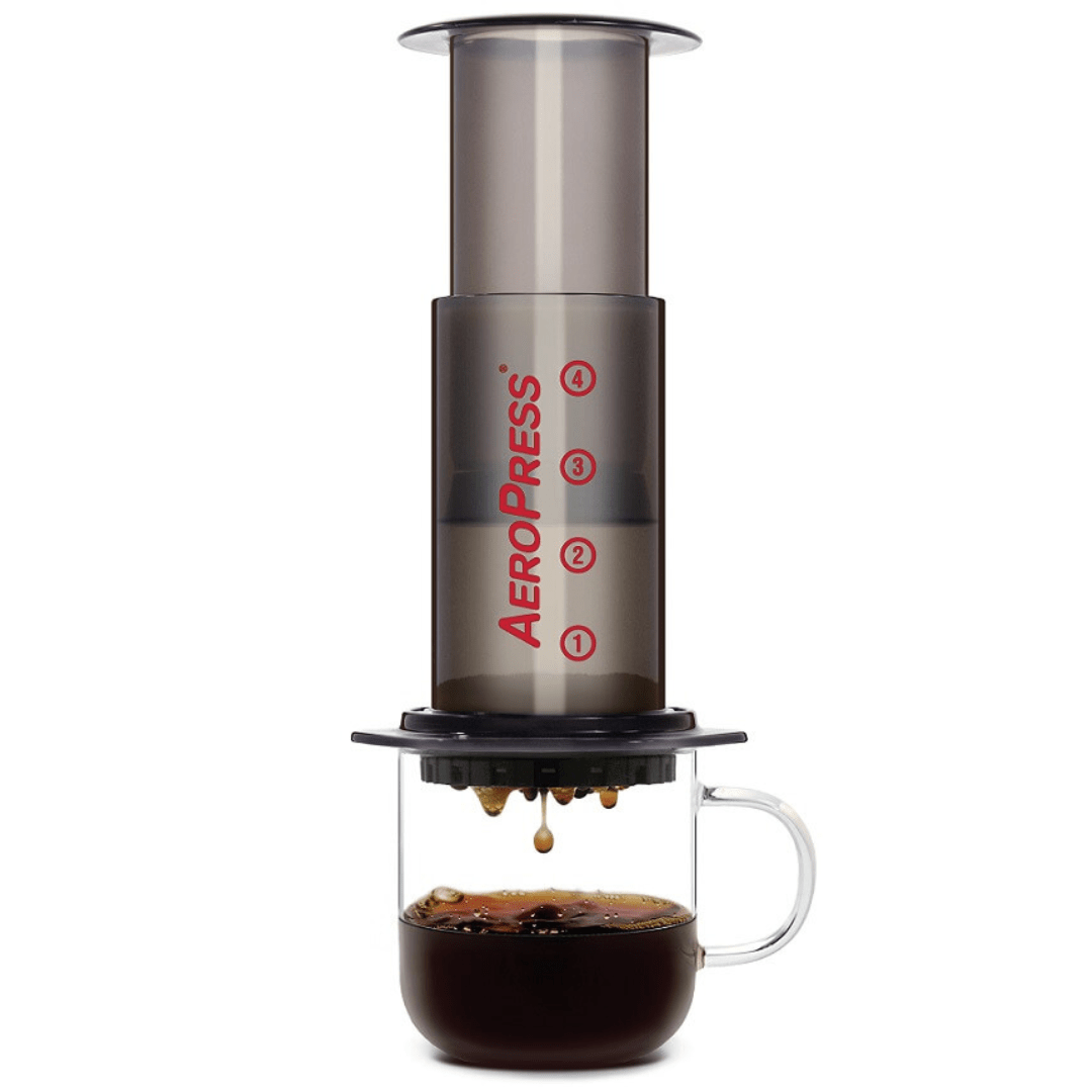 Die AeroPress Original steht aufgebaut auf einer Glastasse und aus dem Filter tropft Kaffee heraus. 