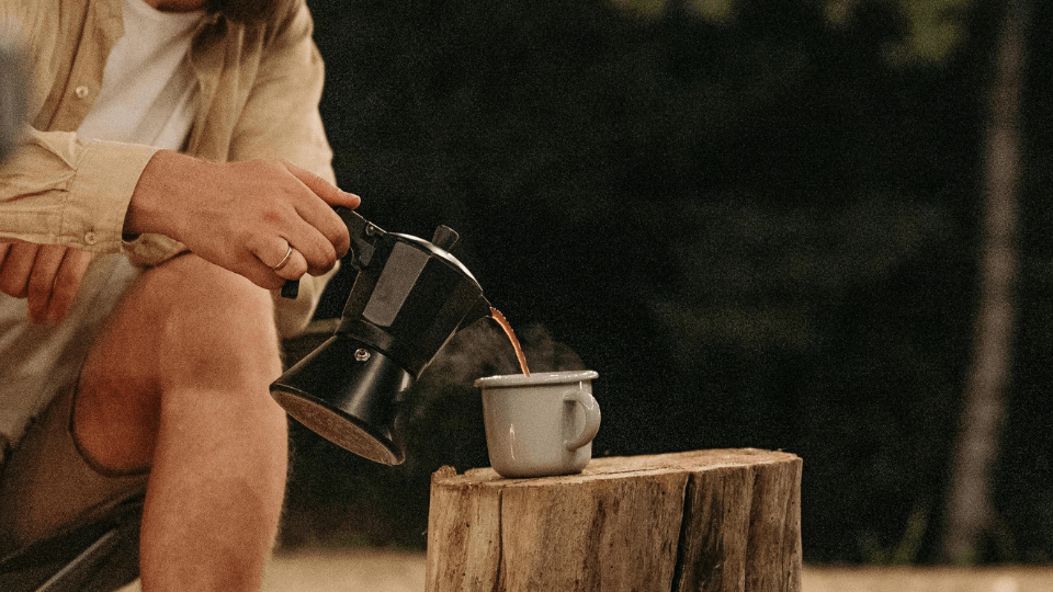Ein Mann kocht frischen Kaffee mit einem Espressokocher in der Natur.