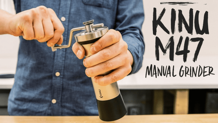 Jemand mahlt Kaffee mit einer Kinu M47 Handmühle, im Hintergrund steht "Kinu M47 Manual Grinder" auf einem Plakat.